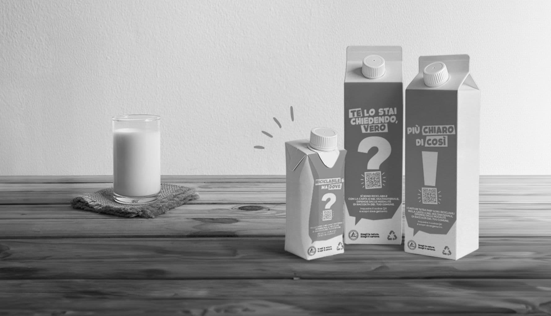 Cartoni Tetra Pak con un punto interrogativo e uno esclamativo accanto a un bicchiere di latte su un tavolo di legno